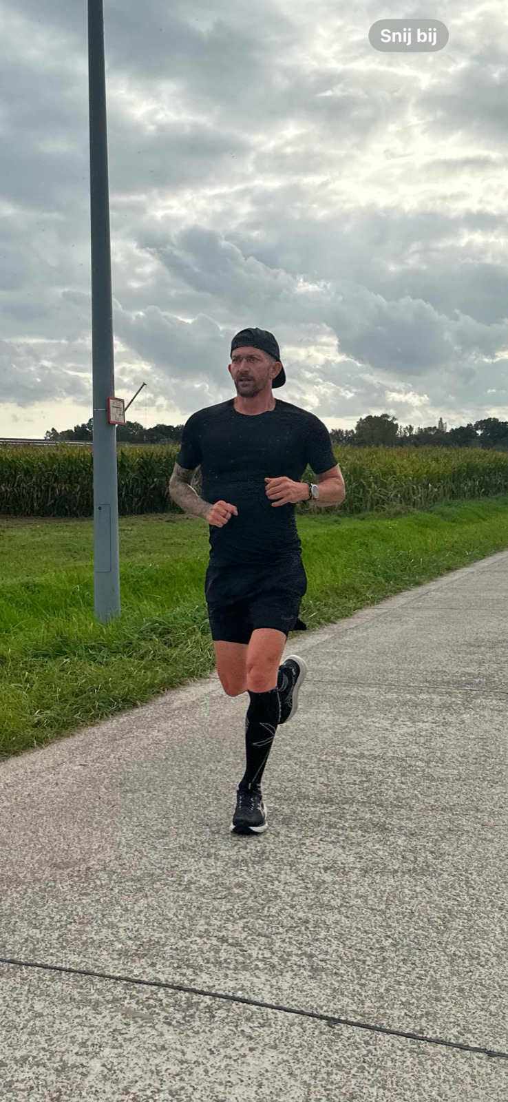 Loper alleen op een betonnen landweg langs een maïsveld